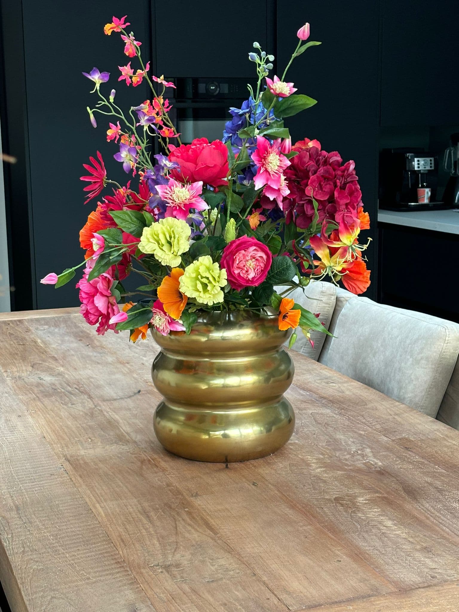 Kleurrijk boeket in een gouden geribbelde vaas op een houten tafel
