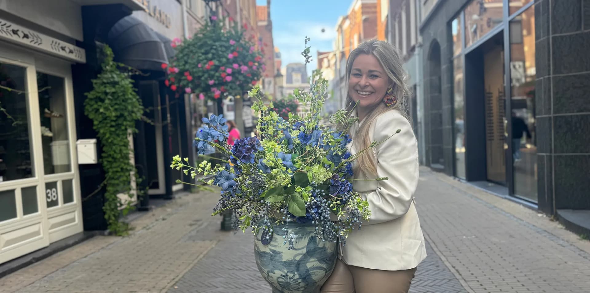 Vrouw met een groot blauw en groen boeket in een blauw-witte vaas in een winkelstraat