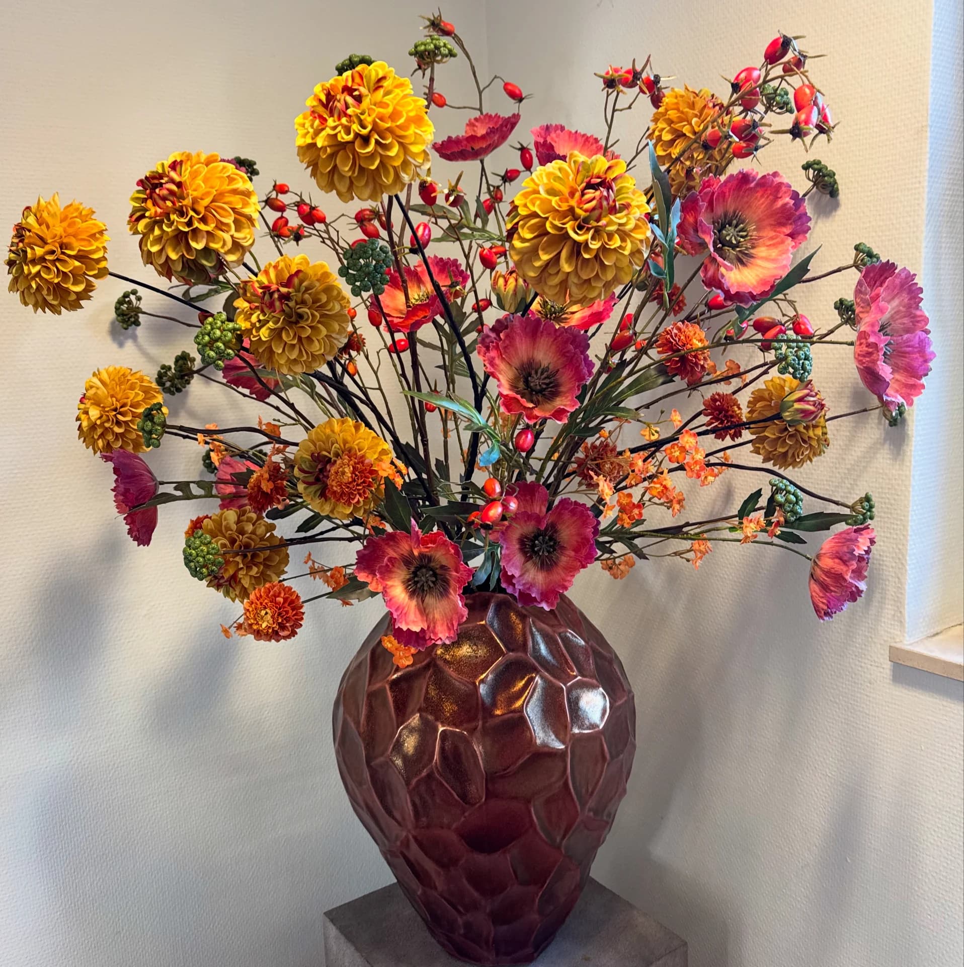 Hoog zijden boeket met oranje dahlia's, rode papavers en rode besjes in een bordeauxrode vaas met reliëf