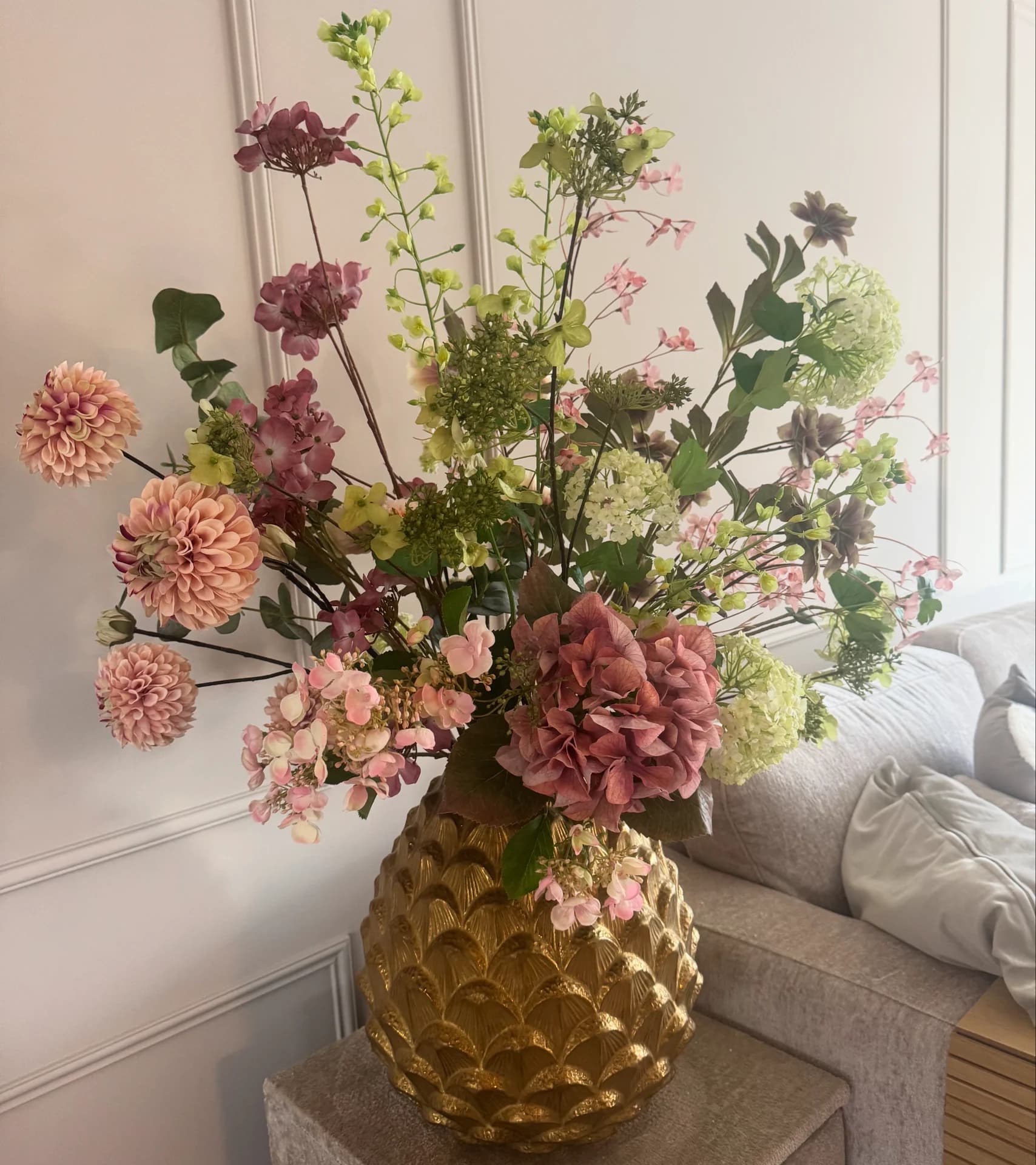 Zijden boeket met oudroze hortensia, roze en groene bloemen in een gouden vaas met schubbenpatroon bij een bank