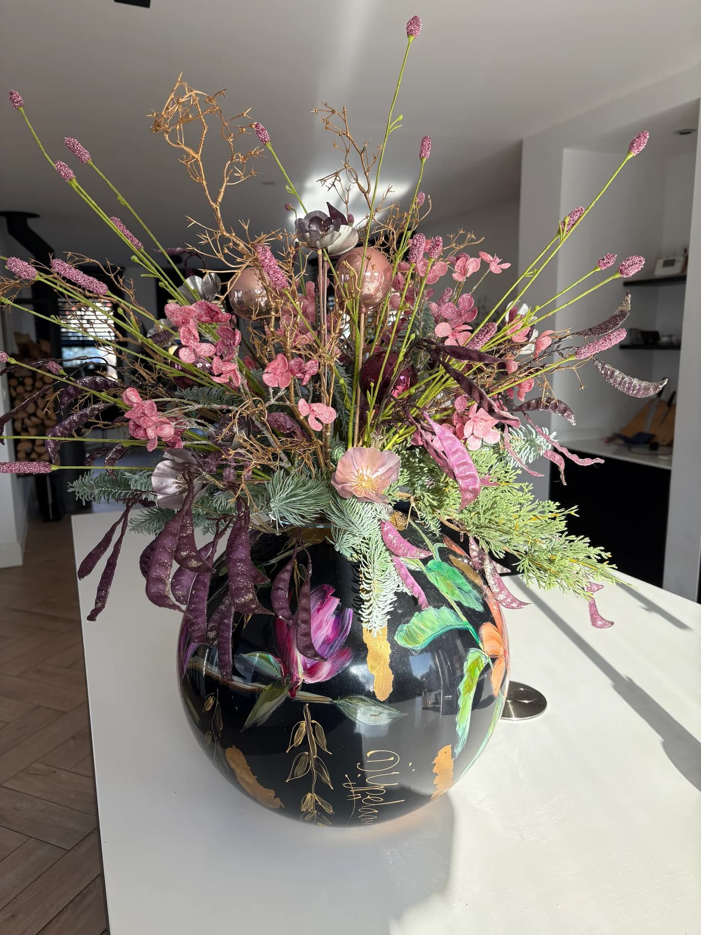Wilde bloemen in roze, paars en groen in een zwarte bolvaas met bloemenprint op een wit keukeneiland