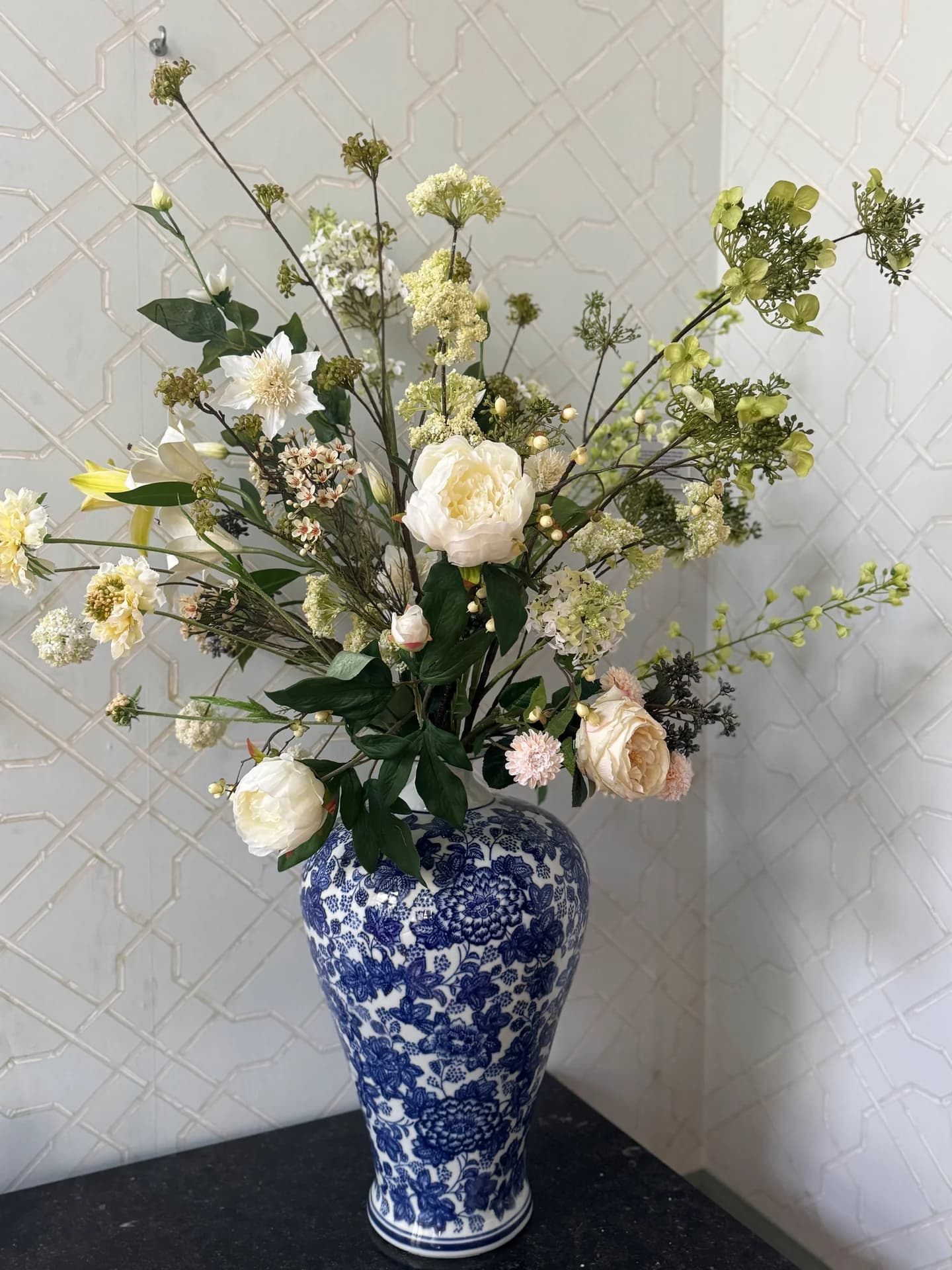 Luchtig boeket met witte rozen en crèmekleurige bloemen in een blauwwitte porseleinen vaas voor een witte tegelwand
