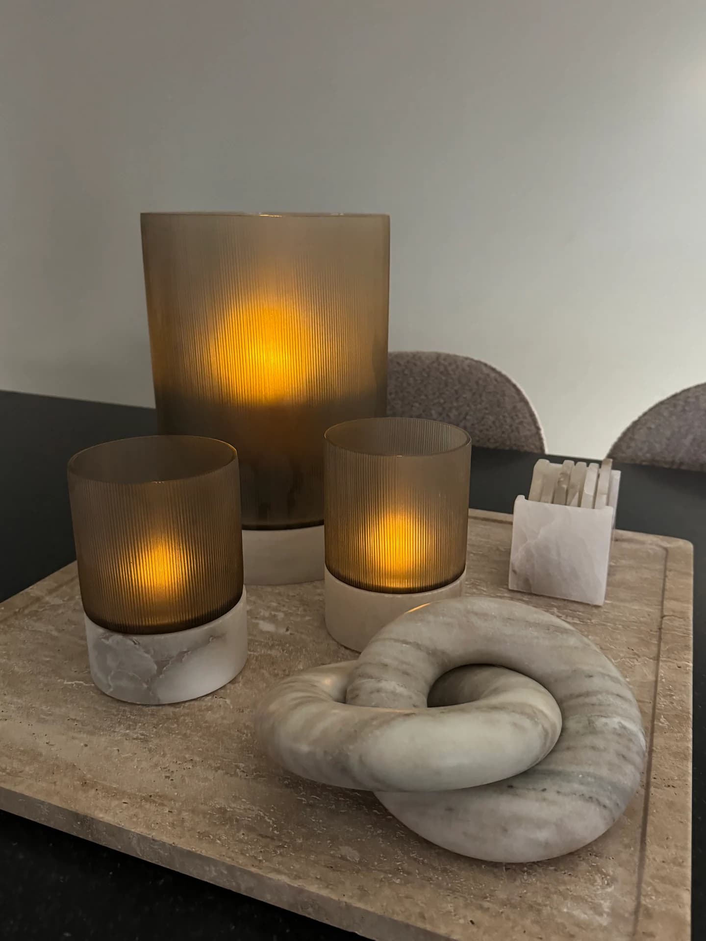 Drie bruine glazen windlichten met lichtjes en een marmeren knoop op een stenen dienblad op tafel